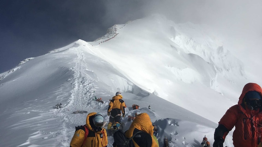 People rugged up in waterproof clothes with a snow-covered peak in the background.