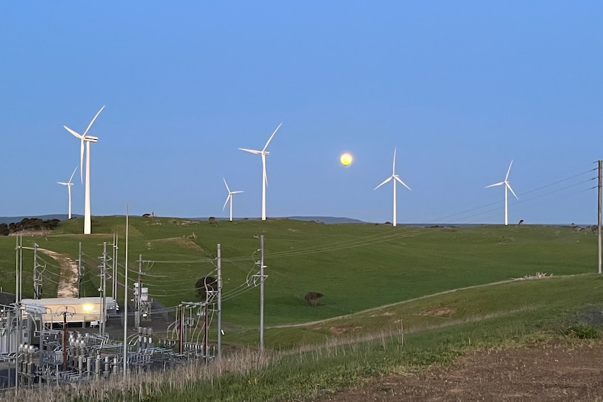 Turbinas eólicas cerca de equipos eléctricos con la luna detrás