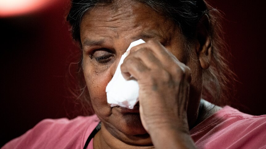 A woman wearing a pink top wipes away tears.