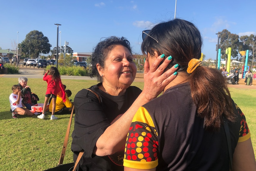 A woman cradles the face of a friend at a suburban park. 