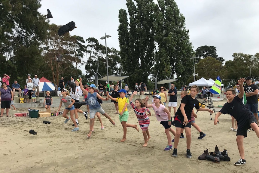 A row of children throw boots in a competition at Sandy Bay, Regatta.