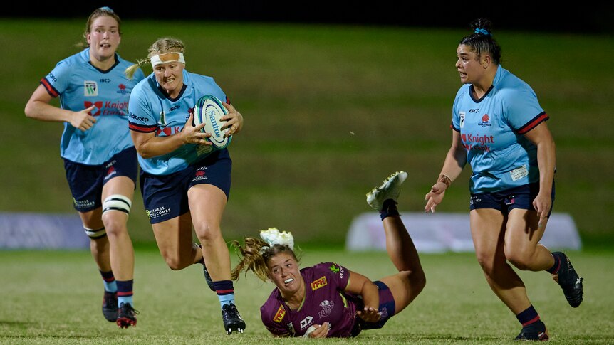 Emily Robinson holds the ball in both hands and runs away from a player lying on the ground looking up at her