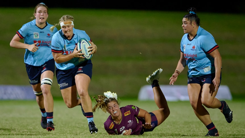 Emily Robinson holds the ball in both hands and runs away from a player lying on the ground looking up at her