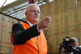 Scott Morrison, dressed in a suit and a high-vis vest, gesticulates as he speaks in a factory.