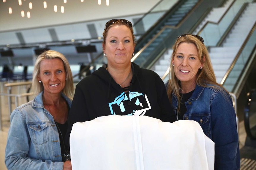 Three women, the middle one holding a large white bridal dress holder.