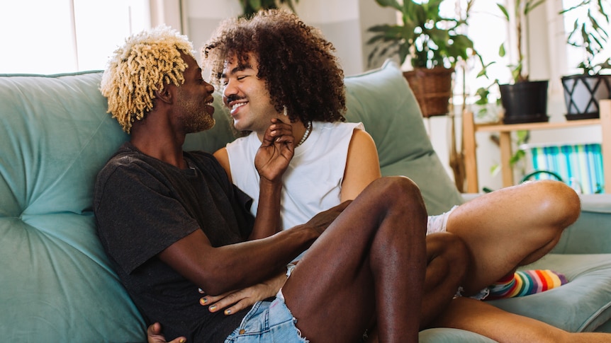 Two loved-up men cuddle up on couch.