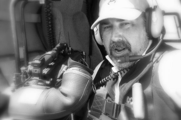 Black and white photo of Drought wearing chopper headset and holding camera.