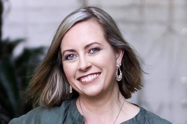 A smiling woman in a green top look into the camera as she poses for a head shot.