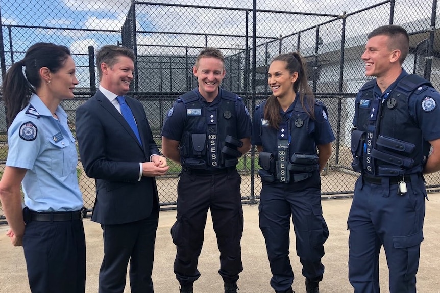 Ben Carroll standing and smiling with two female and two male police officers who are in uniform outside a prison.