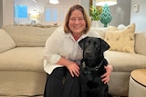 Jaci Armstrong sits on her lounge in her living room hugging her black guide dog