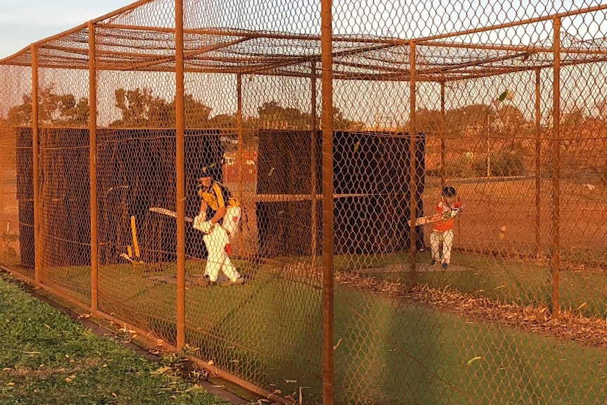 Two young cricket players with bats inside red dust-stained batting nets