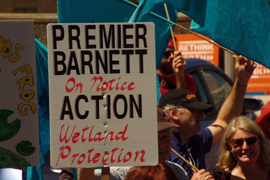 Protesters and a sign reading 'Premier Barnett on notice action wetland protection'.