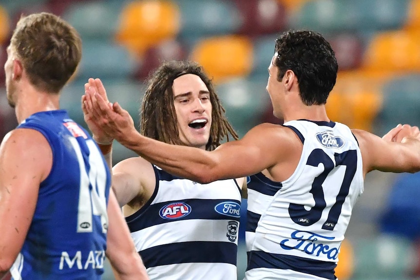 Gryan Miers and Sam Simpson high-ten each other as a North Melbourne opponent walks past