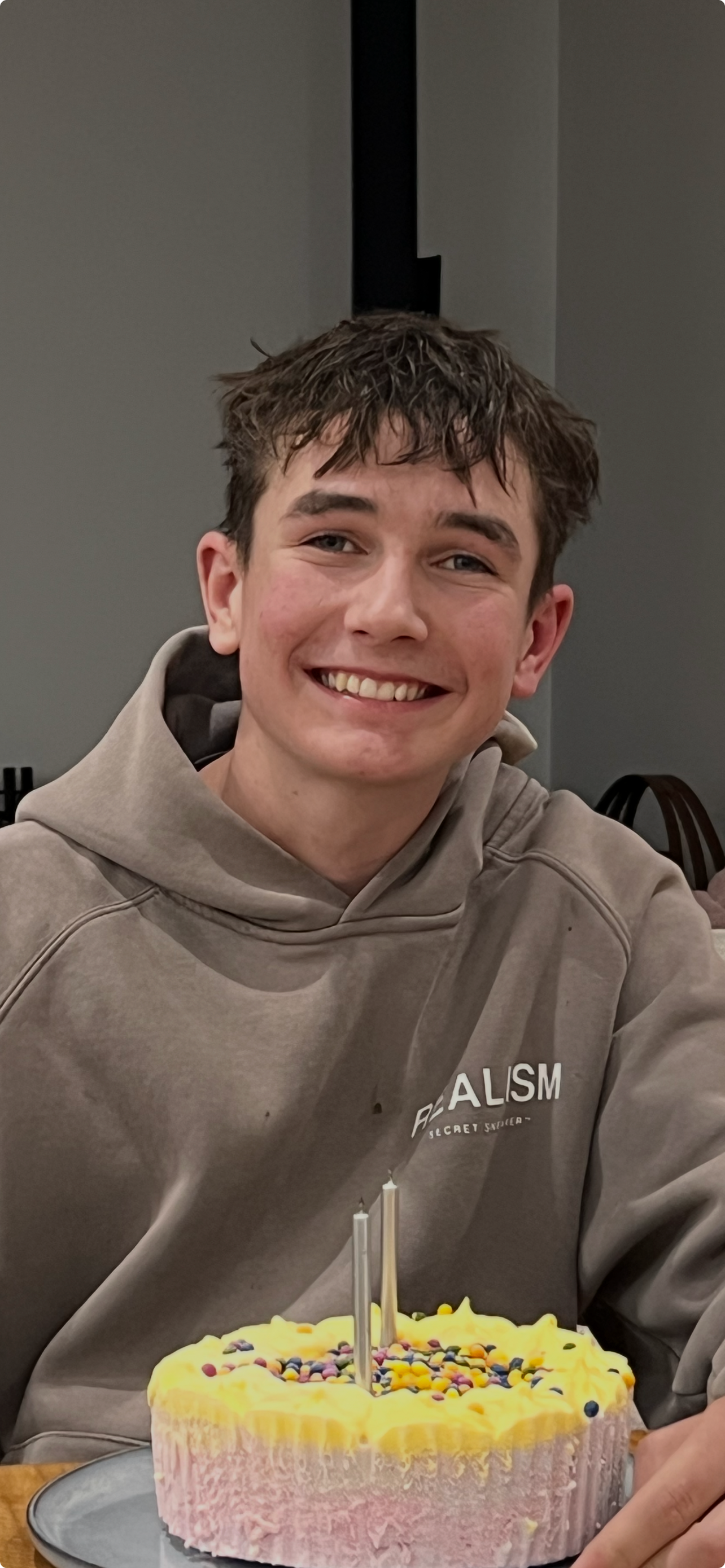 a teenage boy smiles in front of birthday cake on a table