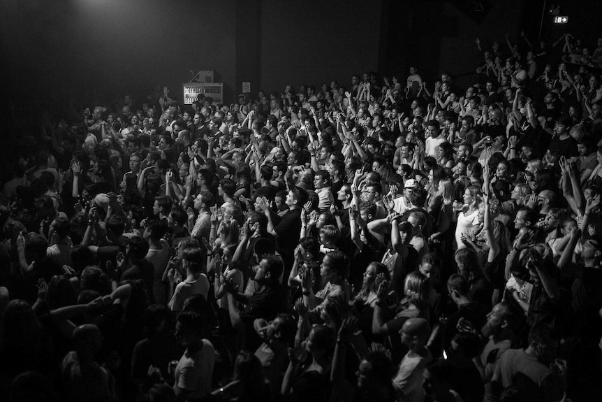 Black and white photo of the crowd at a gig in a venue, applauding and enjoying a night out.