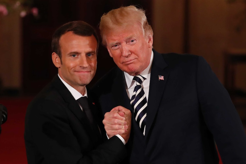 Emmanuel Macron clasps hands with Donald Trump.
