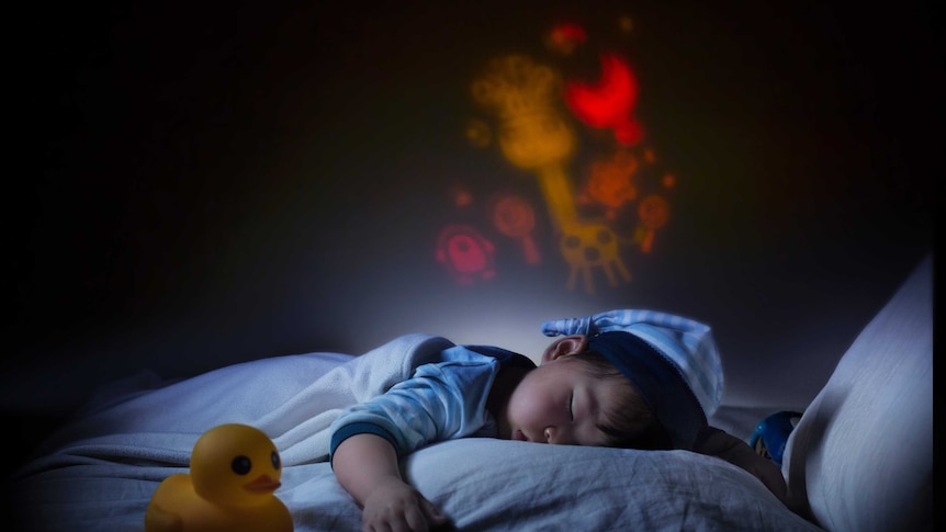 A child sleeping in bed with a night light making patterns over his head.