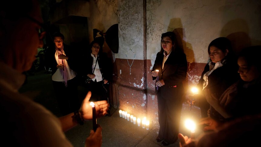 Mourners stand with lit candles next to the youth shelter.