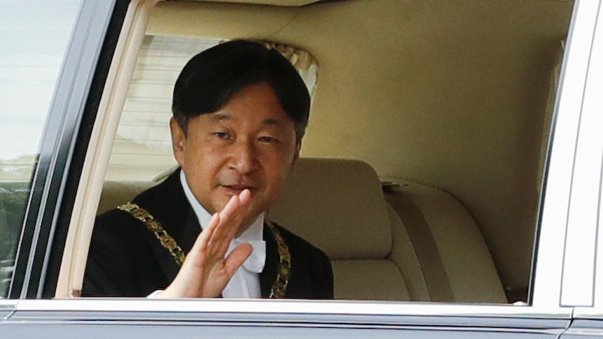 Japanese Emperor Naruhito waves from the back seat of a car as he arrives for his ascension to the throne.