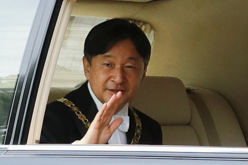 Japanese Emperor Naruhito waves from the back seat of a car as he arrives for his ascension to the throne.