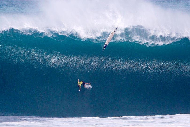 Grant Baker about to land on the bottom of a huge wave, with his surfboard in mid-air high above him.