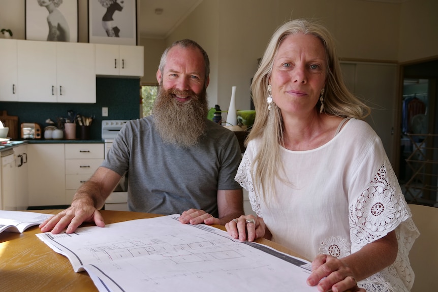 Un homme à la barbe touffue et une femme aux cheveux blonds sont assis à une table et sourient