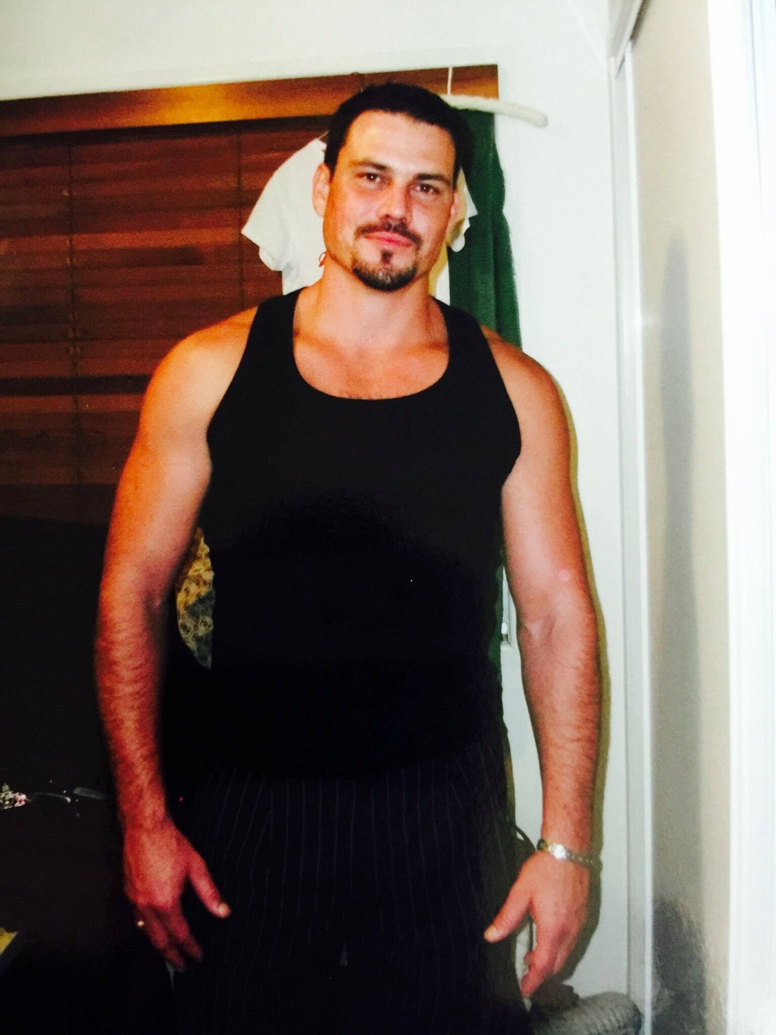 A man with a goatee posing for a photo. He is well built and wearing a black singlet. 