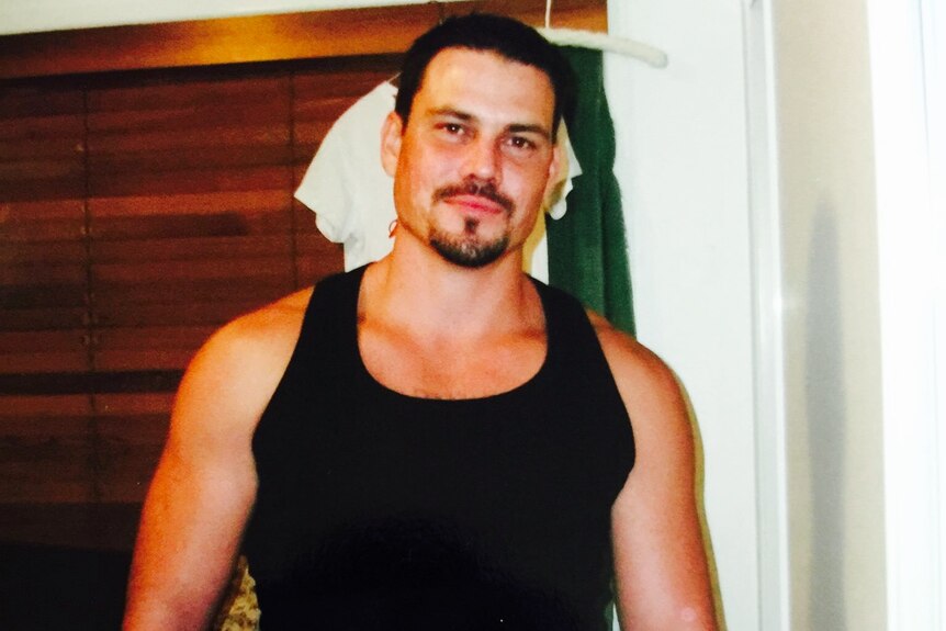 A man with a goatee posing for a photo. He is well built and wearing a black singlet. 