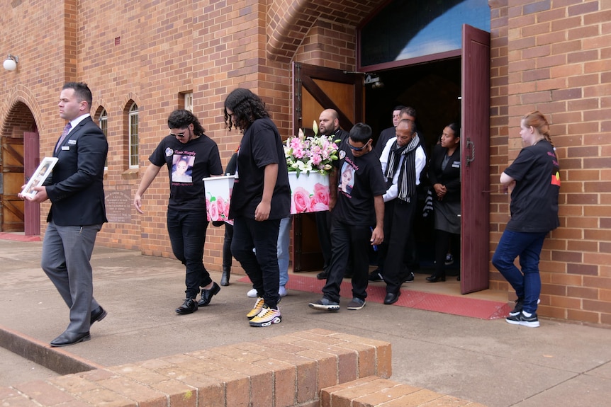 A group of people carry a casket out of a church.