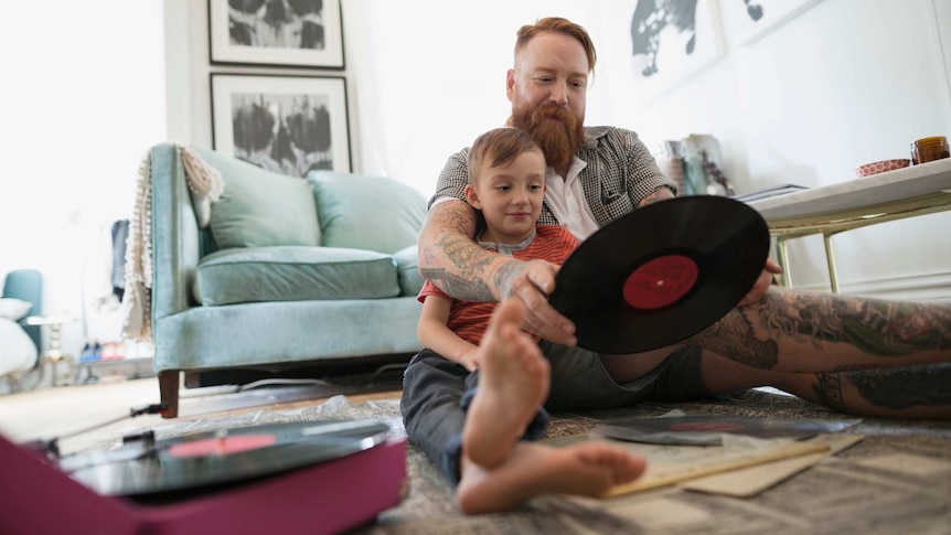 A man and his son look at a record on the floor of their living room