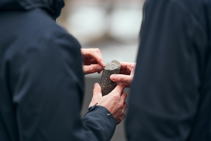 close up of two people holding black cut of basalt rock, which has carbon stored as white crystals
