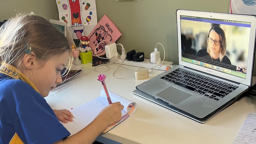 A little girl works at a desk with an iPad on it.