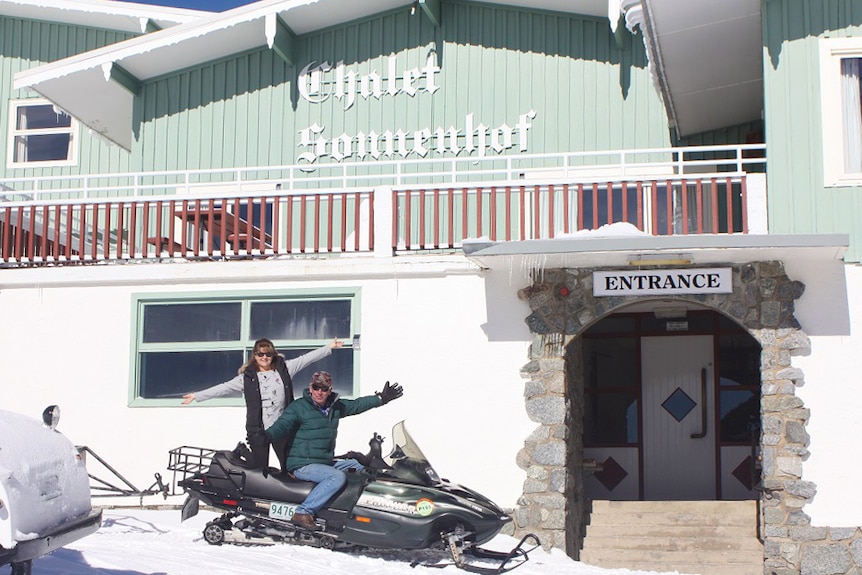 A man and woman on a snow mobile outside a ski lodge.