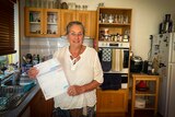 An older woman stands in a kitchen holding a bill