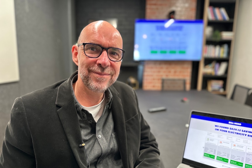 Bespectacled man with shaved head sitting at computer