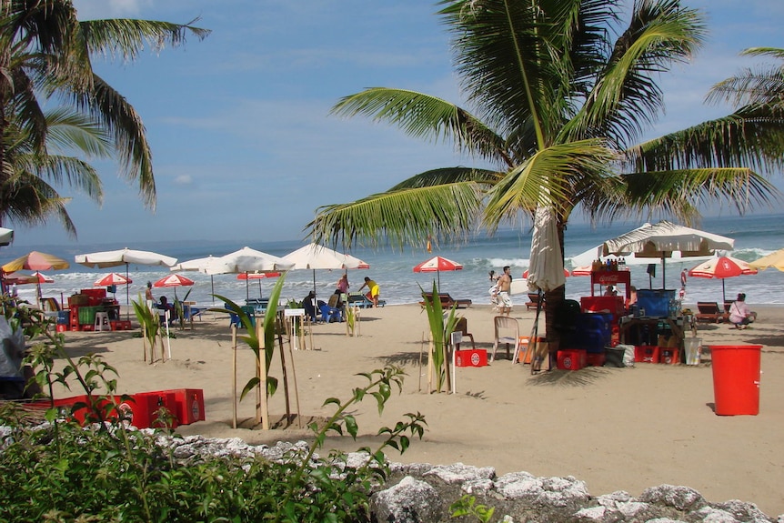 A beach with coconut trees, red beer crates and umbrellas.