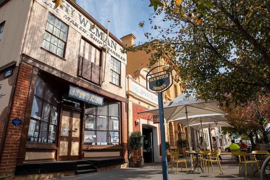 A laneway of colonial buildings with people sitting at cafe tables