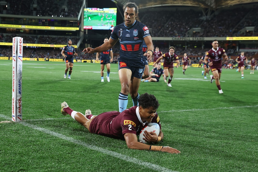 A male Queensland State of Origin player slides over the line to score a try against NSW.