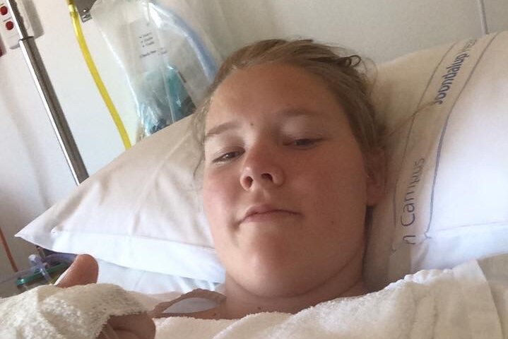 A young blonde woman lying in a hospital bed.