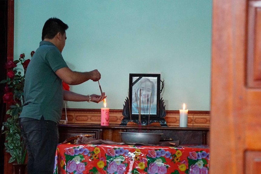 A man lights a candle at an alter that has a photo of a young girl in frame on top of it