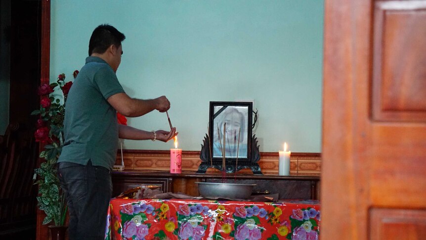 A man lights a candle at an alter that has a photo of a young girl in frame on top of it