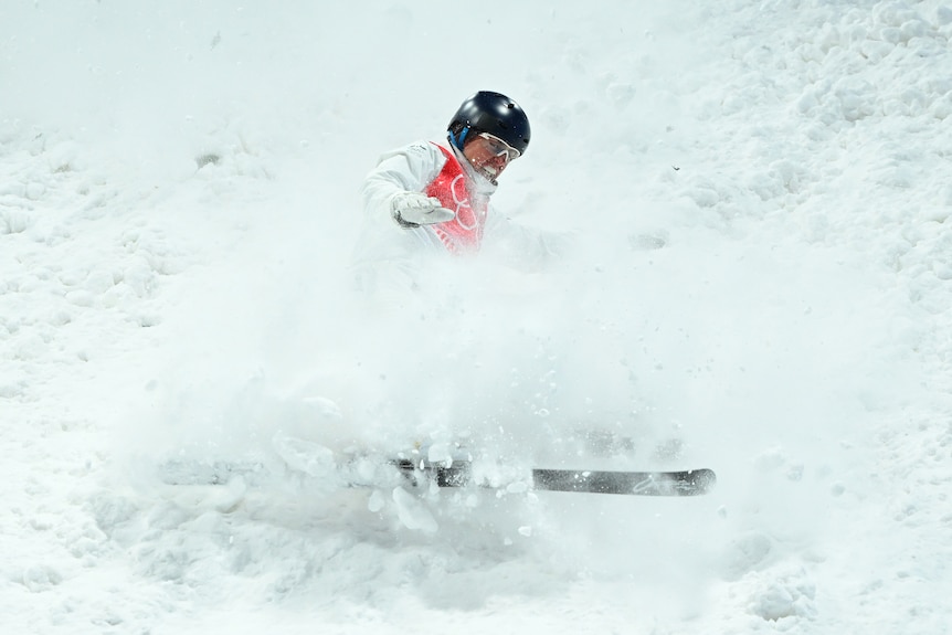 Woman in an aerial jump contest lands in the snow and begins to fall backwards.