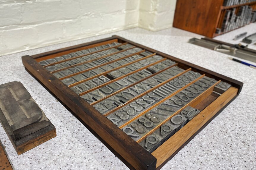 A wooden drawer separated into horizontal sections, old metal type can be seen filling the sections