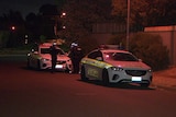 Two police cars parked on the side of the ride with two police officers standing between the cars