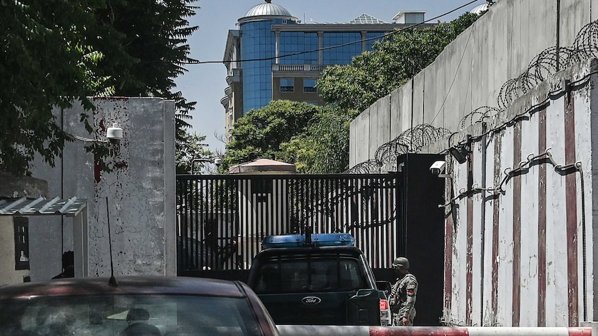 Cars being checked before entering a security gate. High concrete walls and barbed wire