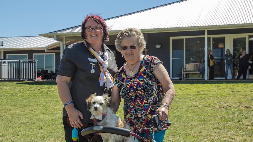 A dog on an aged care walker with a nursing home staff and resident standing behind