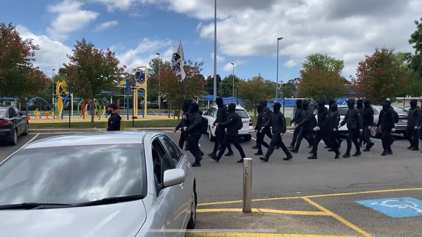 A small group of masked Nazis parading through a carpark.