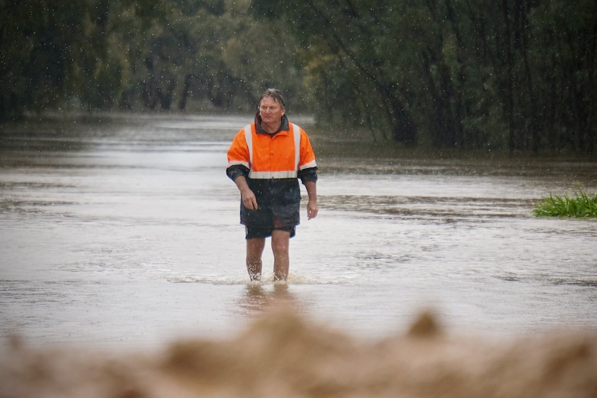 A man walks through floodwater in the rain.
