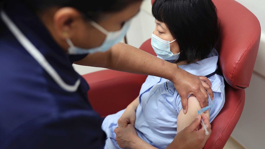A nurse administers a vaccine to a woman wearing a mask.