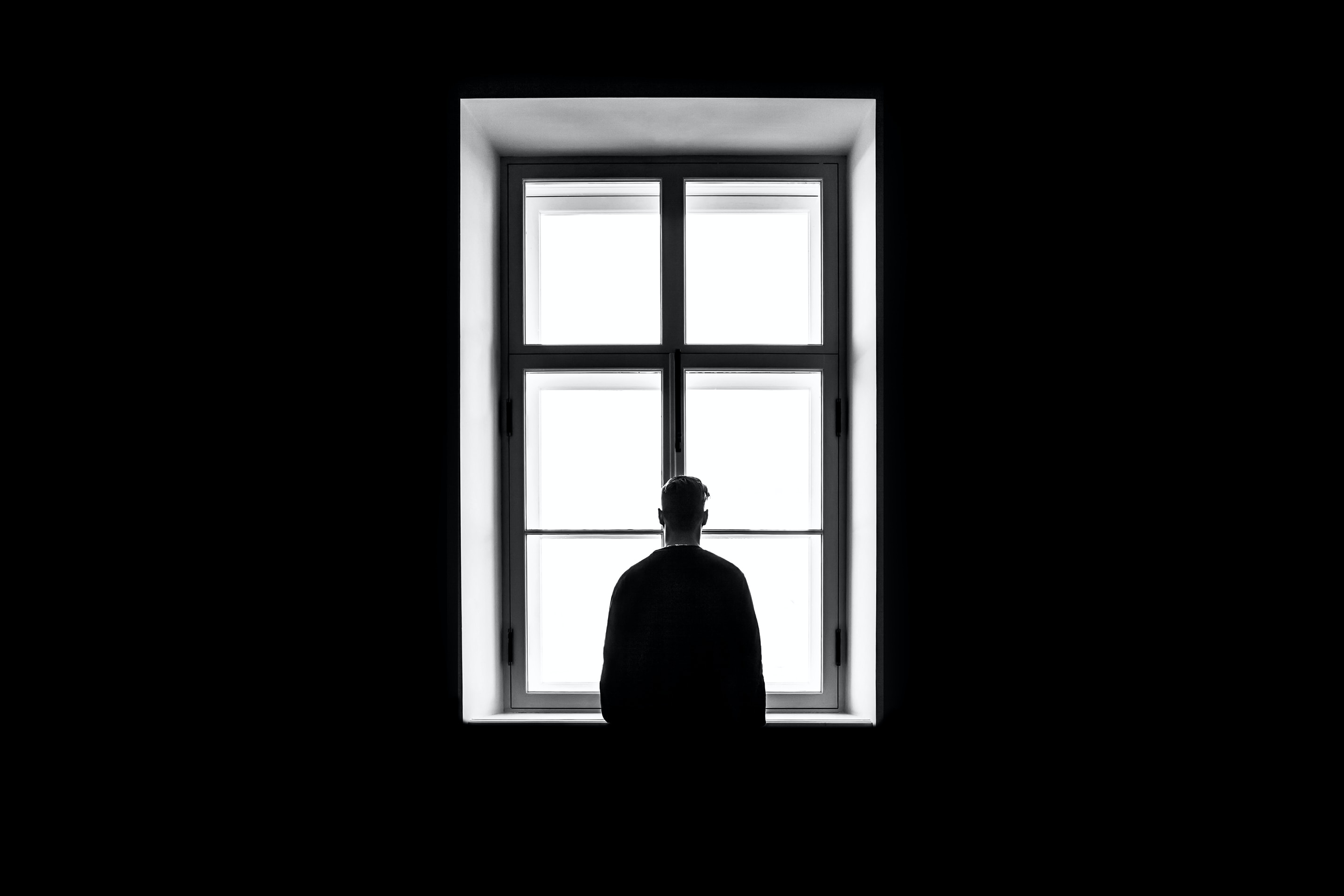 Silhouette of person with short hair standing against a large window with clear expanse.